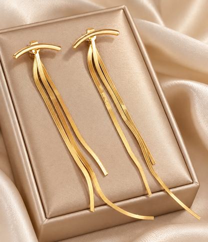 Aretes ráfaga dorada largos y minimalistas de Nia-Vanity, con diseño elegante y acabado brillante sobre fondo neutro.